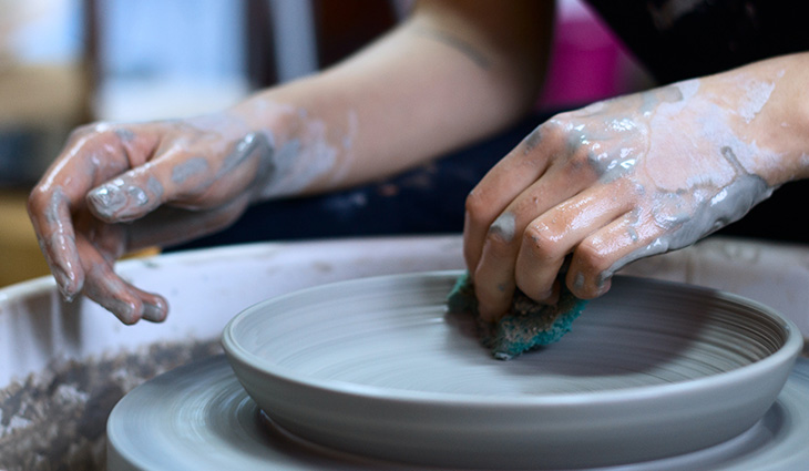 A close up of a student using the pottery wheel