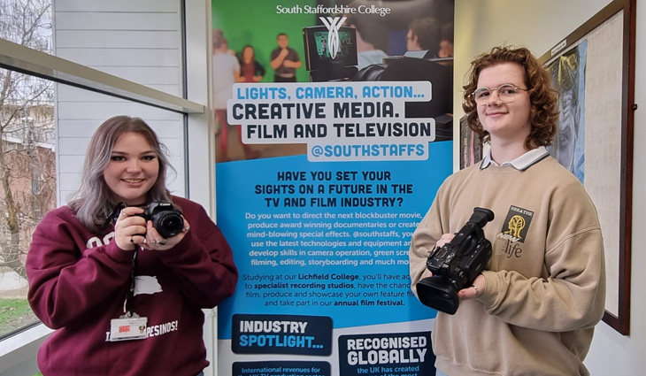 Film students holding cameras and standing in front of banner
