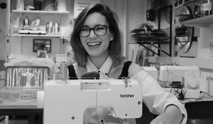 A student smiling using a sewing machine