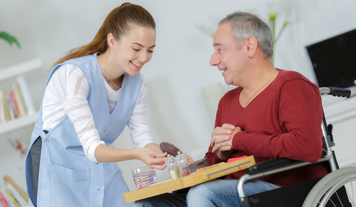 Girl working in care home helping man in wheelchair