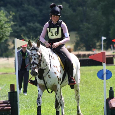 Photograph of Paige Cooper sat on white and brown spotted horse at a competiton