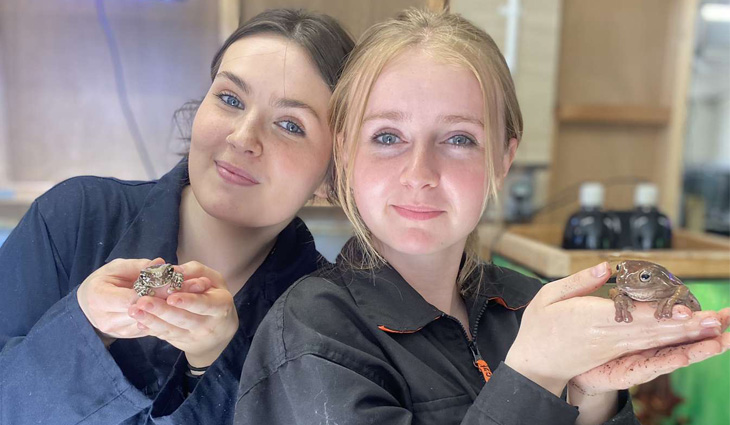 Two female Animal Care students holding frogs