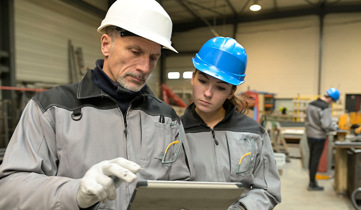 Two people in hard hats looking at an ipad