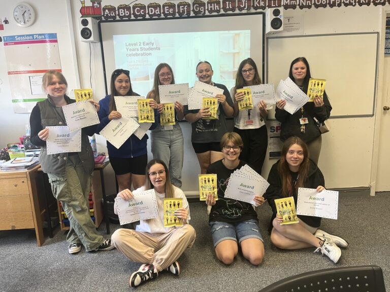 Level 2 Early Years group at Tamworth holding certificates in front of board