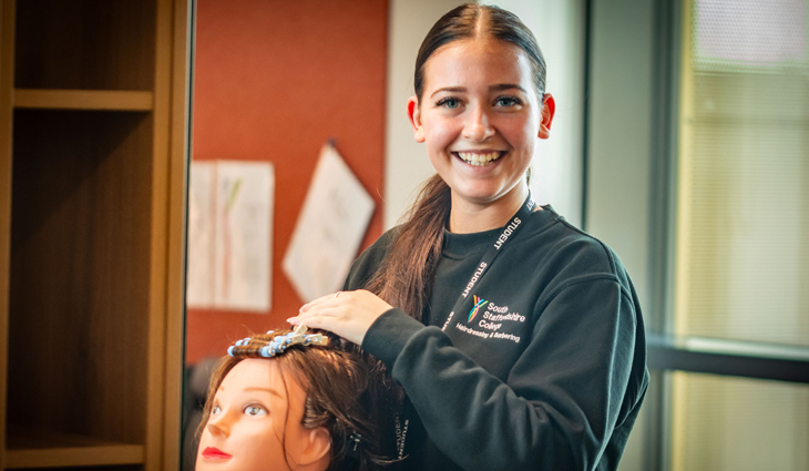 Photo of Level 2 Hairdressing student Katie Crook smiling at camera whilst working on a training head