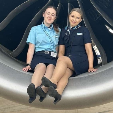 Photo of former Travel and Tourism students Hannah Kemp and Alex Hyde sitting in front of an aeroplane engine working for TUI