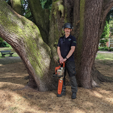 Photo of Jamie Cook standing in front of a tree holding a chainsaw