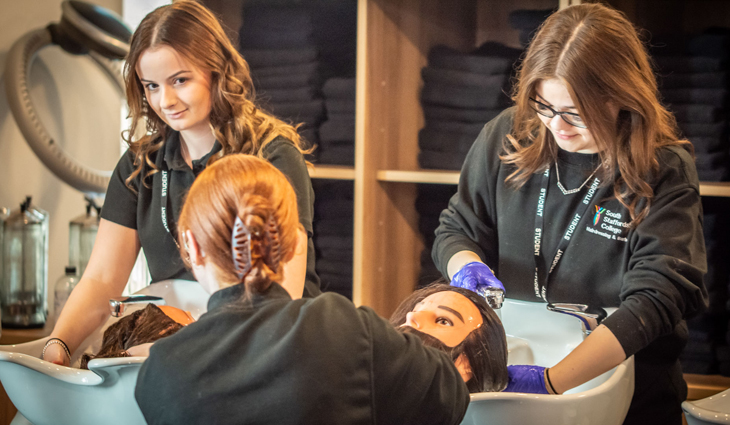 Photo of Level 3 Hairdressing students Hannah Elsmore and Jessica Owen, and Level 2 Barbering student April Weller, washing training heads in sinks