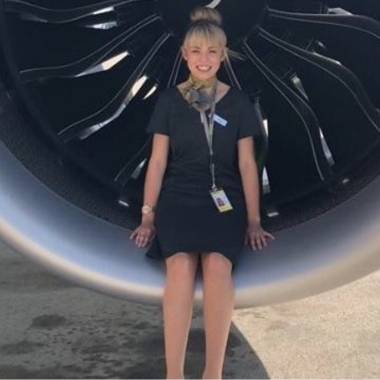 Photo of former Travel and Tourism student Megan Latham sitting in front of an aeroplane engine working for Primera Air
