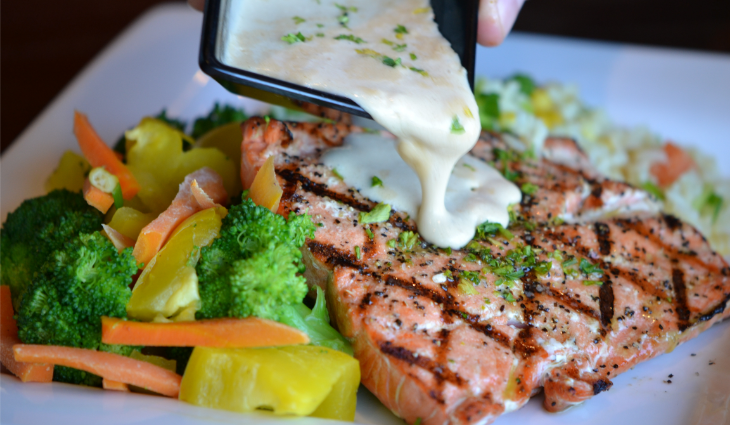 Person pouring sauce on salmon