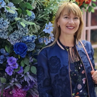 Photo of lecturer Olena Volkova standing in front of flower wall