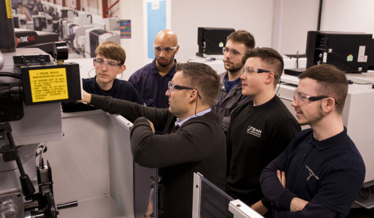 Group of learners around engineering machine with teacher