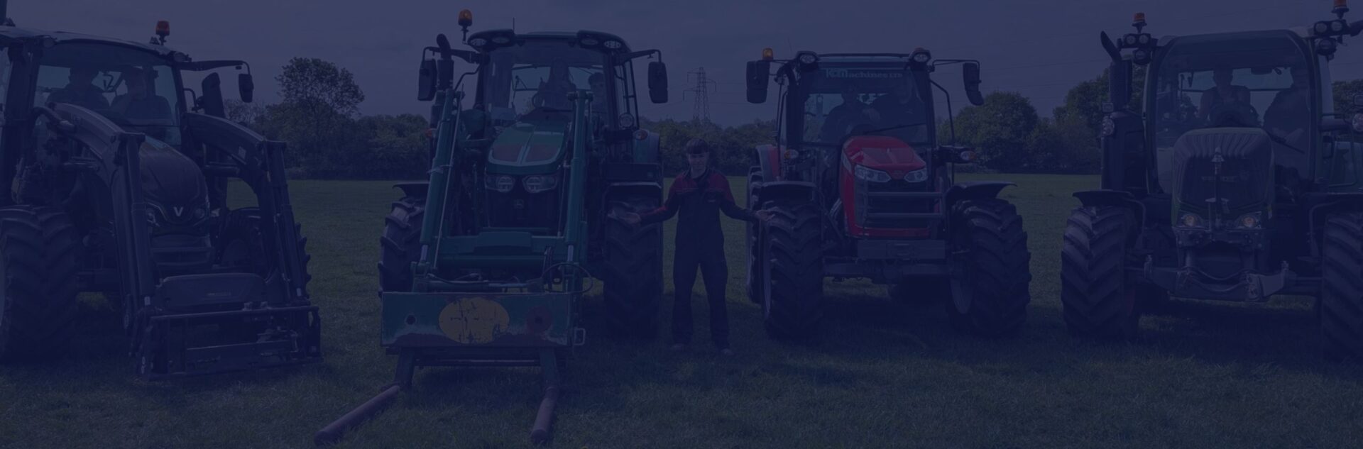 Male student stood with 4 tractors in a field