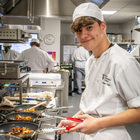 A male student in the kitchen cooking chicken in a pan